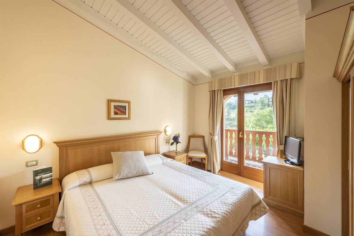A bedroom with a bed, bedside table, lamp, and a TV on a stand.