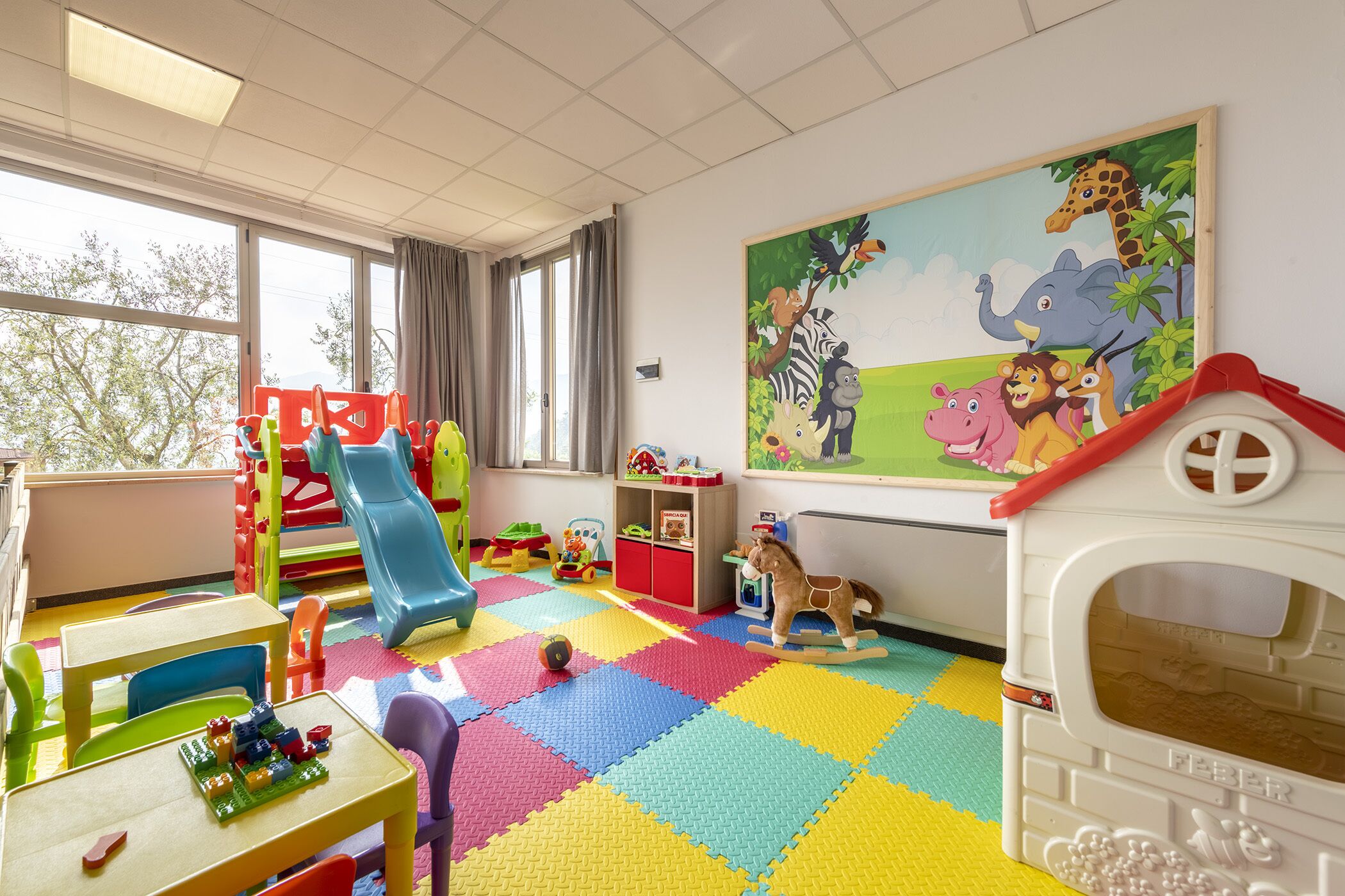 A children's playroom with colorful play mats, a slide, and various toys.