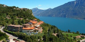 A hillside hotel with multiple buildings, a swimming pool, and a view of a lake and mountains. - Residence Pineta Campi (Tremosine)