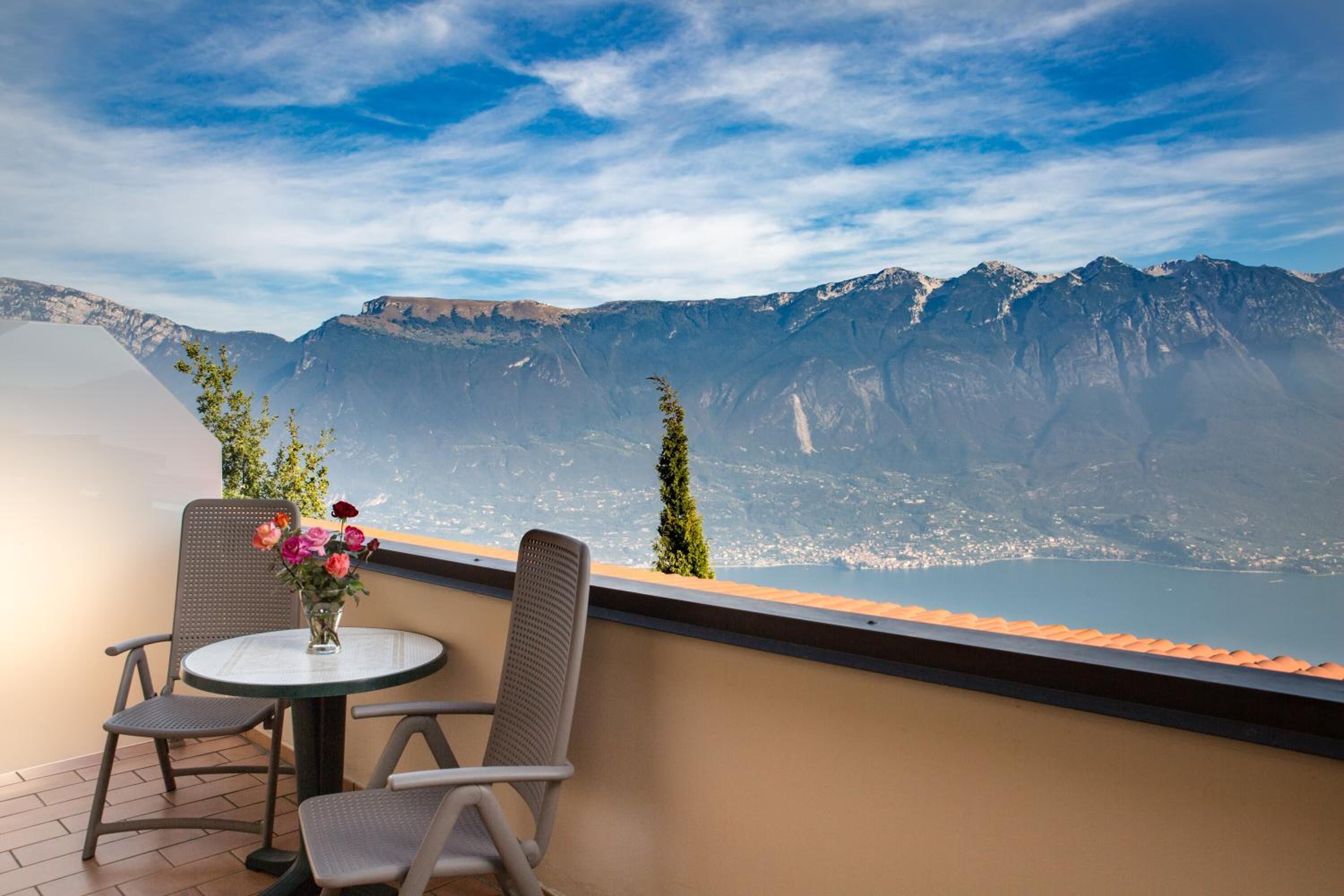 Un balcone con due sedie e un tavolo, affacciato su un paesaggio montuoso con un lago.