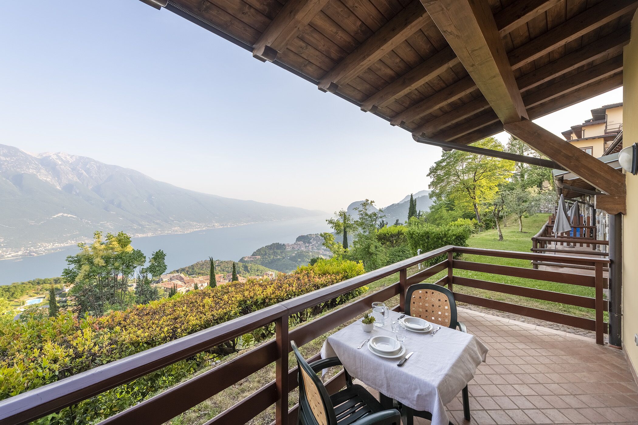 A terrace with a table set for two, overlooking a mountainous landscape and a lake.