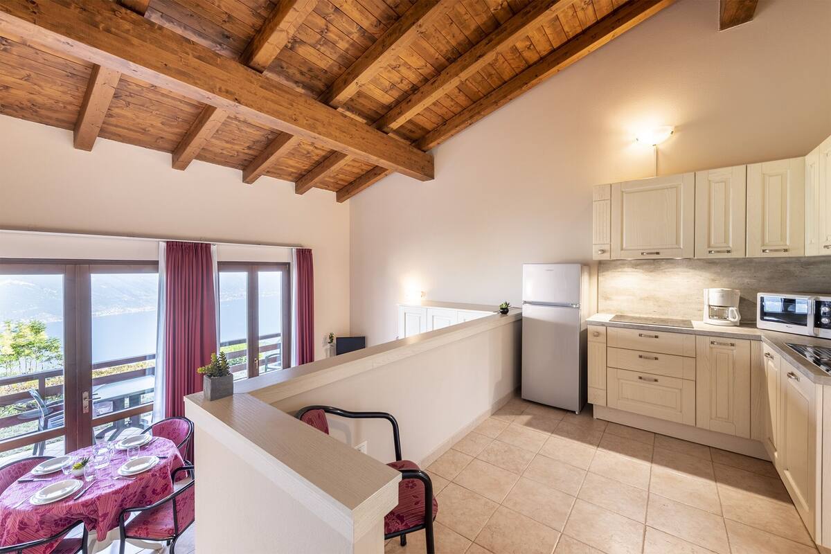 A kitchen with wooden beams, a dining area with a table set for four, and a view of the outdoors.