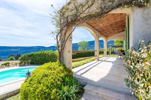Ein Poolbereich mit einer Pergola, Sitzgelegenheiten im Freien und Blick auf die Berge.
