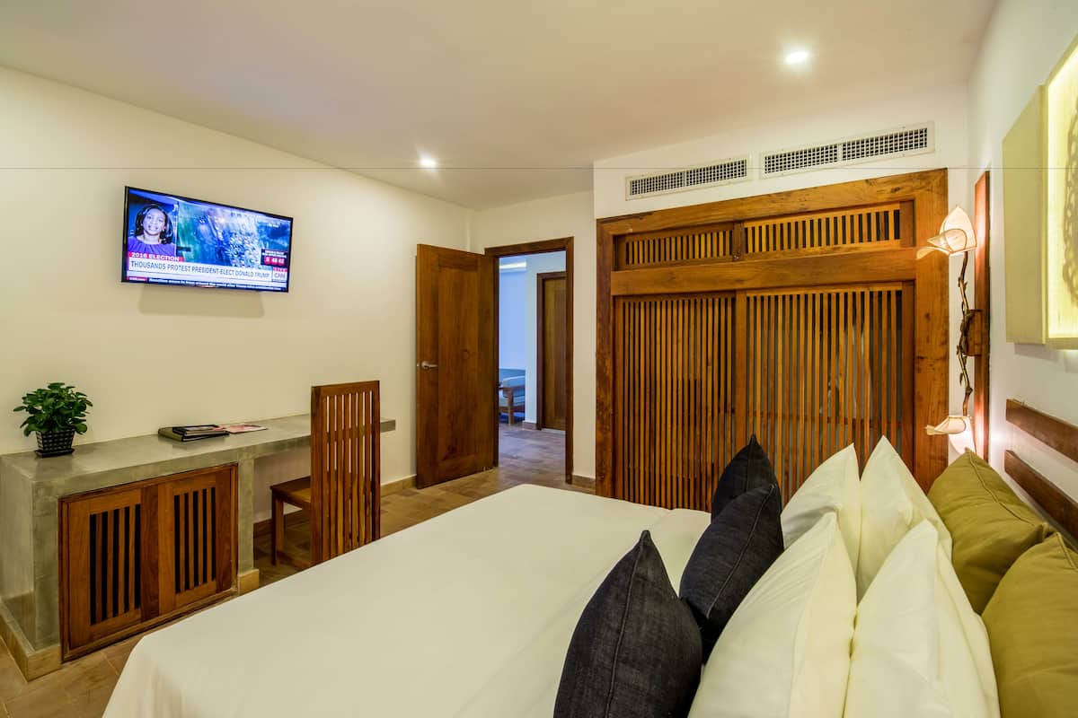 A bedroom with a bed, a TV mounted on the wall, a desk, and a wooden wardrobe.