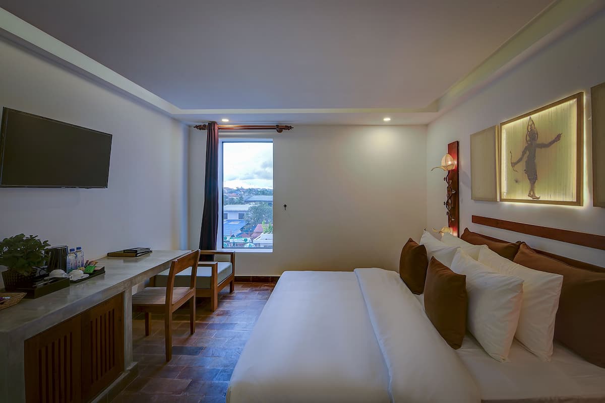 A hotel room with a bed, a desk, a chair, a TV, and a window with a view of the city.