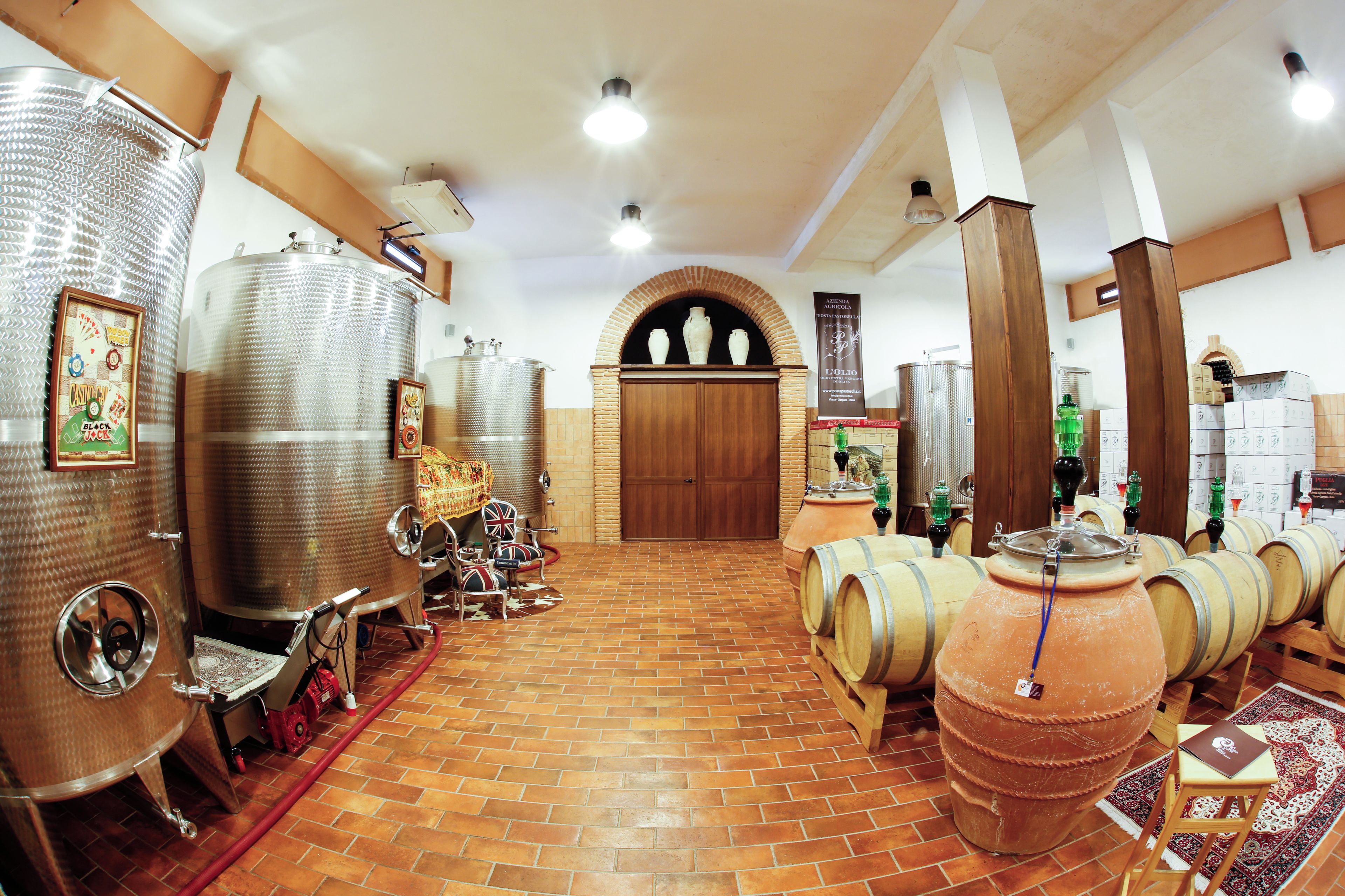 Una bodega con tanques de fermentación de acero inoxidable, barricas de madera y piso de ladrillo.