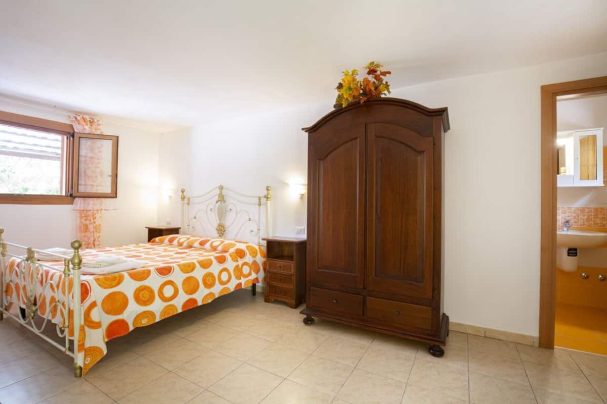 A bedroom with a bed, a wooden wardrobe, a nightstand, and a window with curtains.