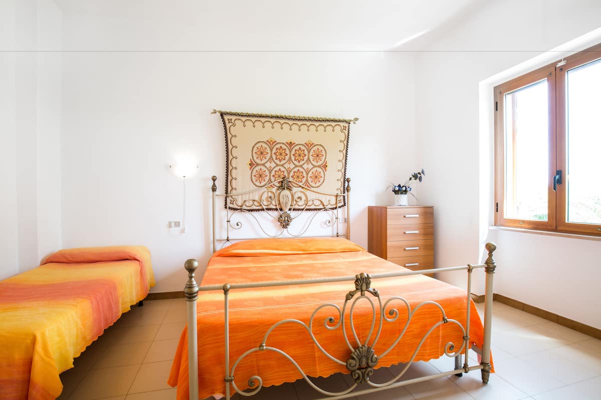 A bedroom with a bed, a nightstand, a dresser, and a window.