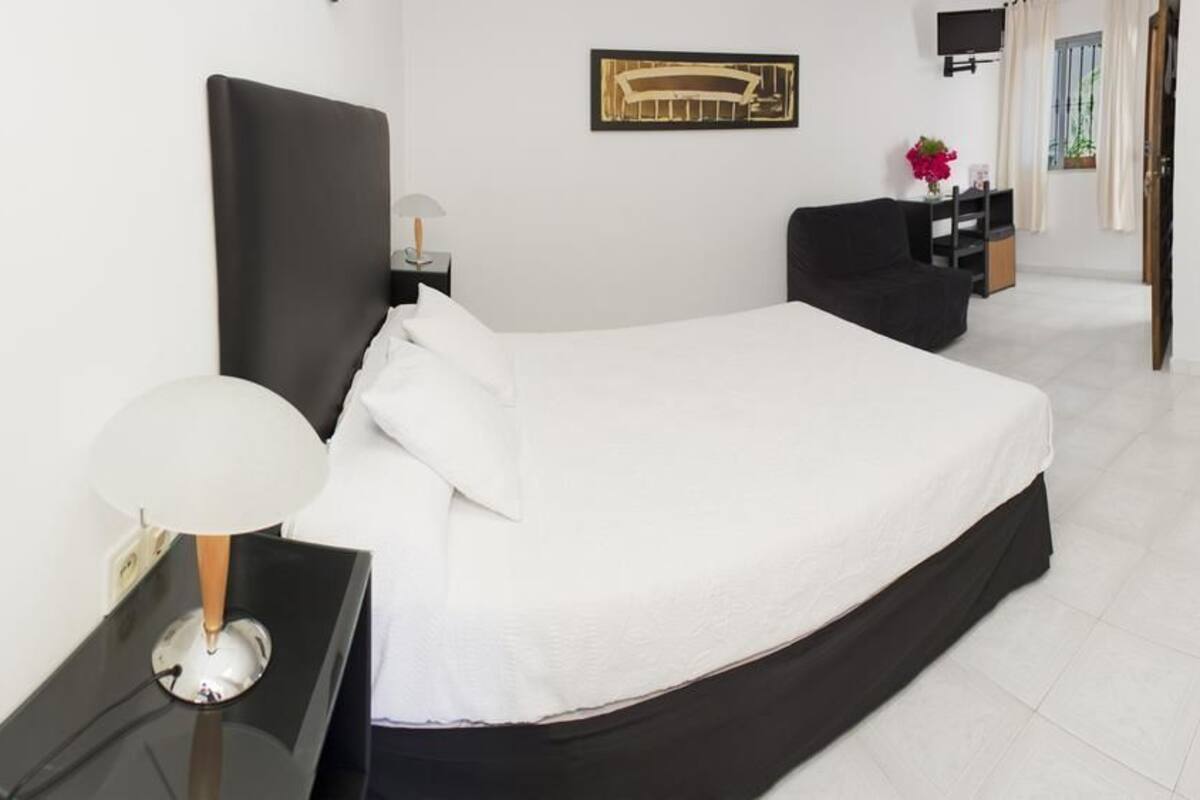 A hotel room with a large bed, a bedside table with a lamp, a TV on the wall, and a view of the hallway.