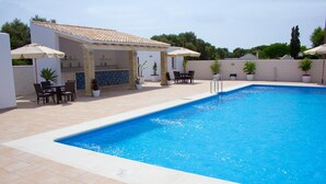Una piscina con solárium azulejado, mobiliario exterior y plantas en macetas.