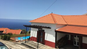 Una casa con techo de tejas rojas, piscina y vista al océano.