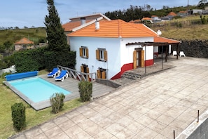 A two-story house with a swimming pool, a patio with lounge chairs, and a stone wall.
