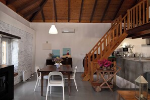 A dining area with a wooden table, white chairs, and a vase with flowers. A wooden staircase leads to an upper level.