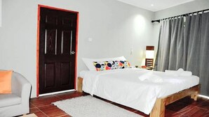 A bedroom with a bed, a chair, a door, and a window with curtains. - La Nature Apartments (Mahé Island)