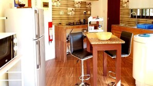 A compact kitchen with a refrigerator, stove, and a small dining area with a table and chairs. - La Nature Apartments (Mahé Island)