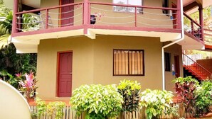 A two-story building with a balcony, a red door, and a window with vertical blinds. - La Nature Apartments (Mahé Island)
