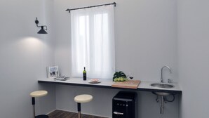 Eine kleine Küche mit Fenster, einer Spüle, zwei Barhocker, einer Flasche und einer kleinen Pflanze.