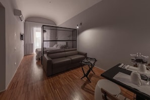 A modern hotel room with a sofa, a dining table, and a bed with a metal frame. - Lidia Chambres D'hotes (Matera)
