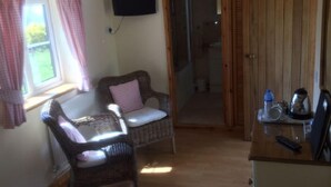 Una stanza con una poltrona in vimini, un tavolino con un bollitore e una televisione appesa al muro.
