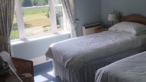 Una camera da letto con due letti, una finestra con tende, un comodino con lampada e vista su un paesaggio verde.