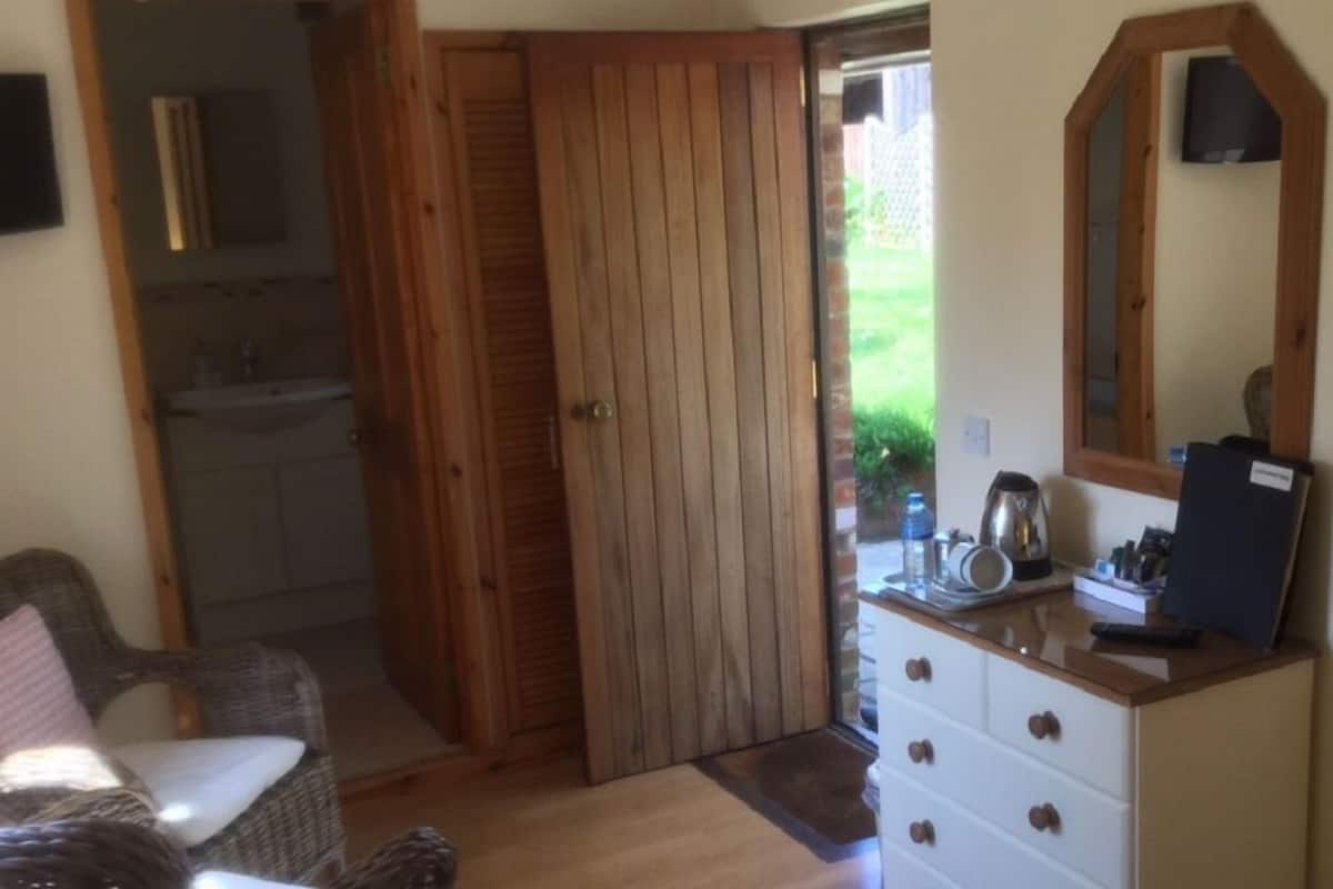 Una habitación con puerta de madera, una silla de mimbre, un aparador blanco con cajones y un espejo en la pared.