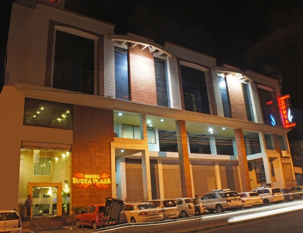 A hotel with a modern facade, multiple entry points, and a parking area with several cars. - Hotel Surya Plaza (Kota)