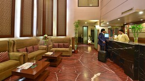 Un vestíbulo de hotel con una recepción, sofás, una mesa de centro y plantas decorativas.