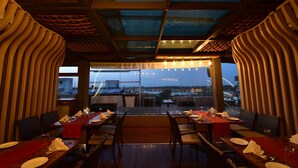 Un comedor interior con mesas dispuestas para dos personas, con vistas a la ciudad a través de amplios ventanales.
