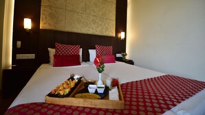 Una habitación de hotel con una cama bien hecha, una bandeja con aperitivos, un florero con flores y una mesita de noche con una lámpara.