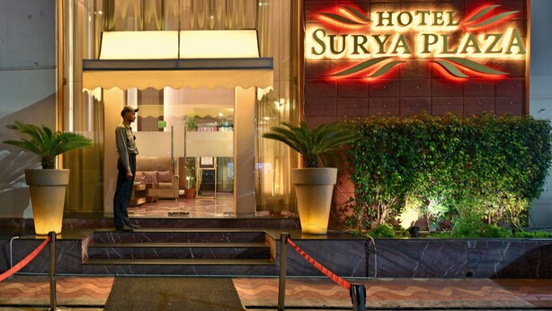 La entrada del Hotel Surya Plaza, con un gran letrero iluminado, escalones que conducen a la entrada y plantas en macetas.