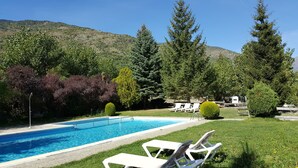 Piscina con sillones de descanso y montañas al fondo.