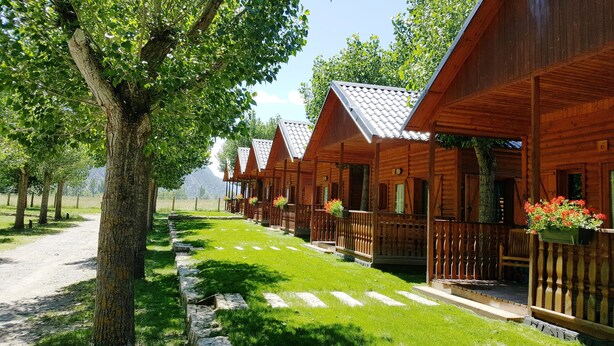 Una hilera de cabañas de madera con balcones, un sendero de piedra y un camino bordeado de árboles.