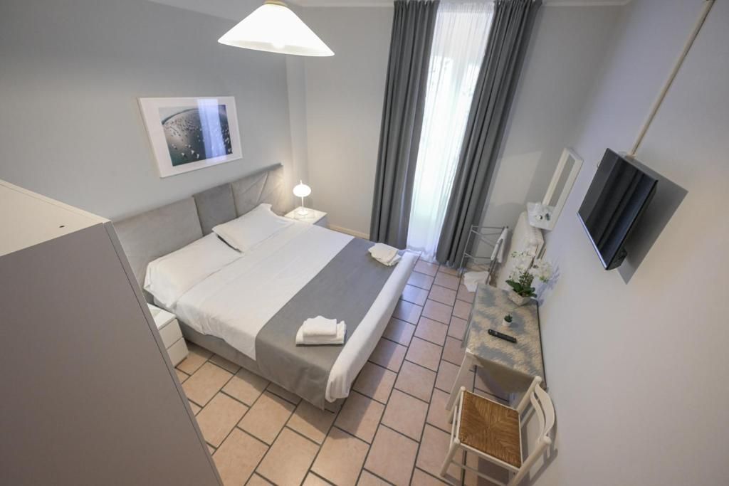 A hotel room with a bed, bedside table, lamp, TV, and a window with curtains.