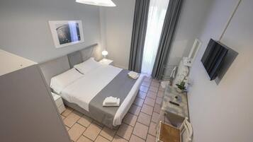 A hotel room with a bed, bedside table, lamp, TV, and a window with curtains.