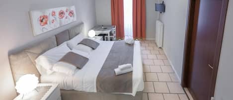 A hotel room with a bed, bedside table, lamp, artwork, and a view of the outside.