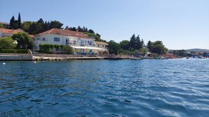 Une propriété située au bord de l’eau, avec un mur en pierre, un bâtiment doté d’un toit en tuiles et un ciel d’un bleu limpide.