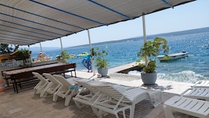 Une terrasse en bord de mer avec des fauteuils blancs, une table et des plantes en pot.