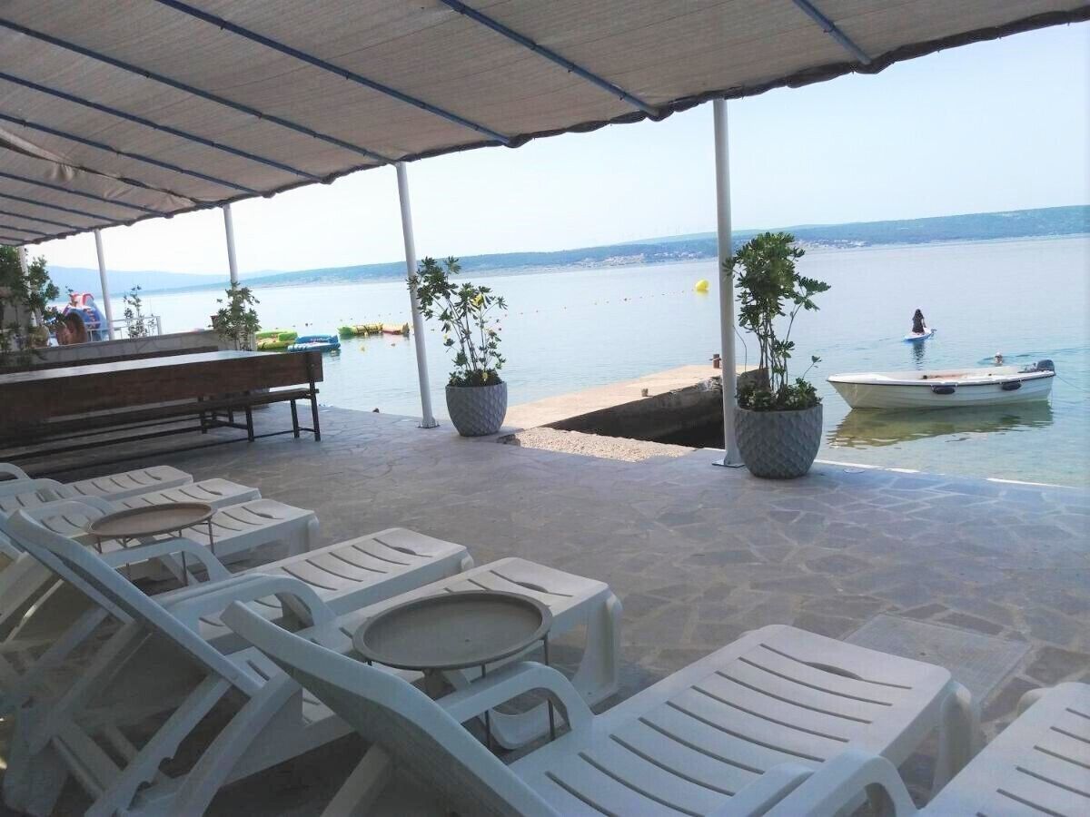 Ein überdachter Außenbereich mit Lounge-Möbeln, Tischen, einer Bar und Blick auf das Wasser.