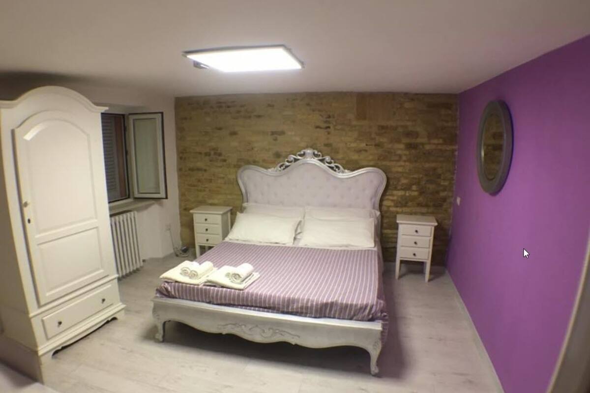 Un dormitorio con cama, mesitas de noche, armario y pared de ladrillo.