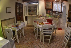 A dining area with a table set for four, surrounded by white chairs. There is a kitchen area with cabinets and a window above the sink. - B&B La Lanterna (Fermo)