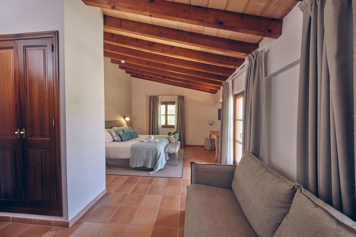 A bedroom with a bed, a nightstand, a window with curtains, a wooden ceiling, and a door.
