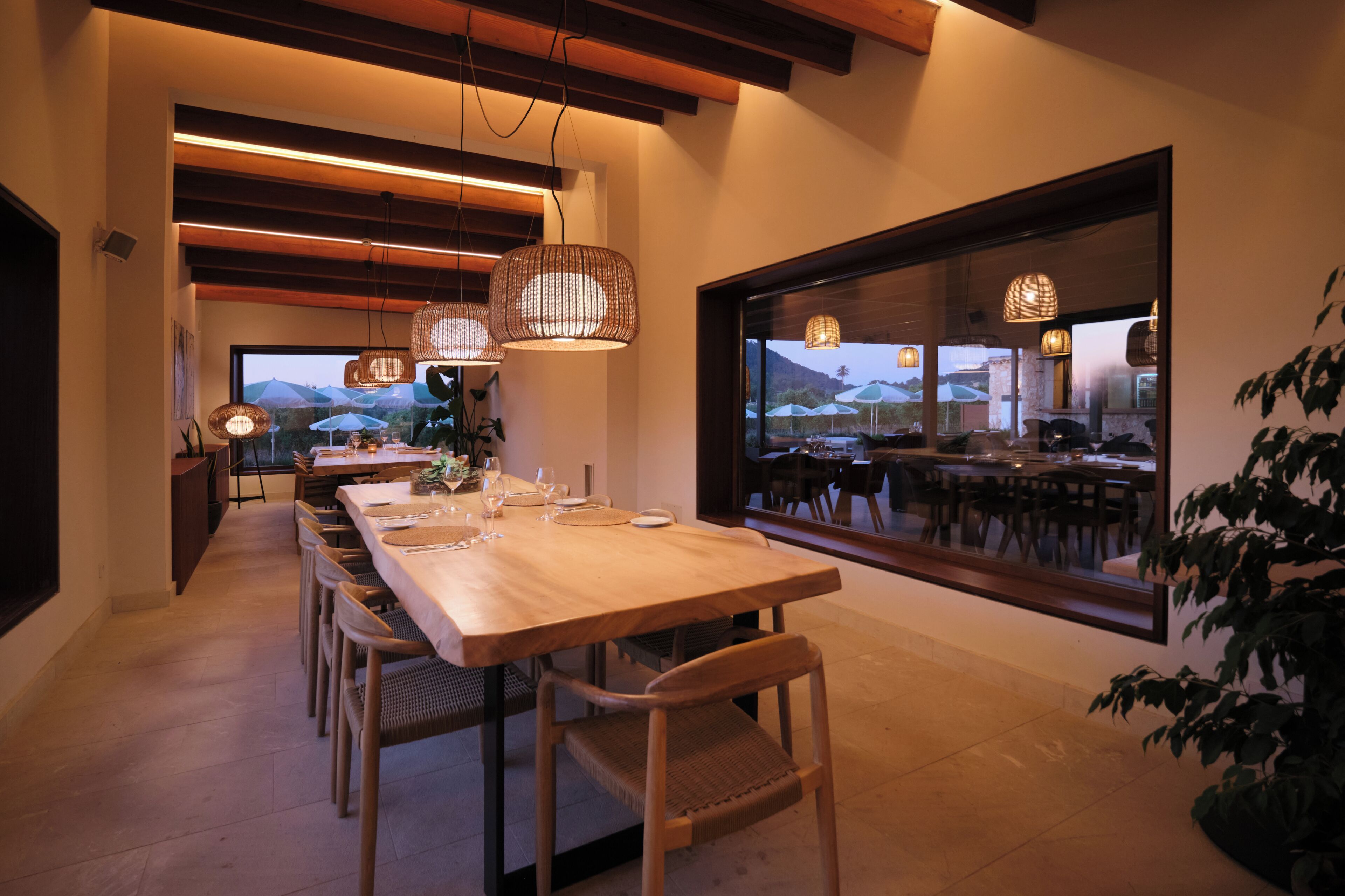 Un comedor con una mesa larga, sillas, luces colgantes y un amplio ventanal con vistas.