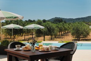 A dining table with outdoor seating, a pool, and a view of a hilly landscape.