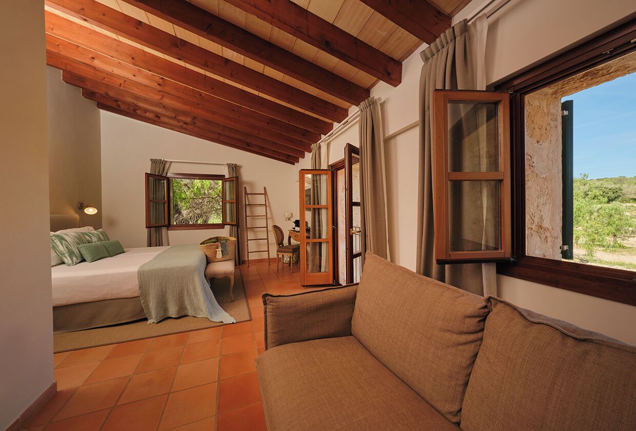 Un dormitorio con cama, sofá, escritorio y ventana con cortinas.