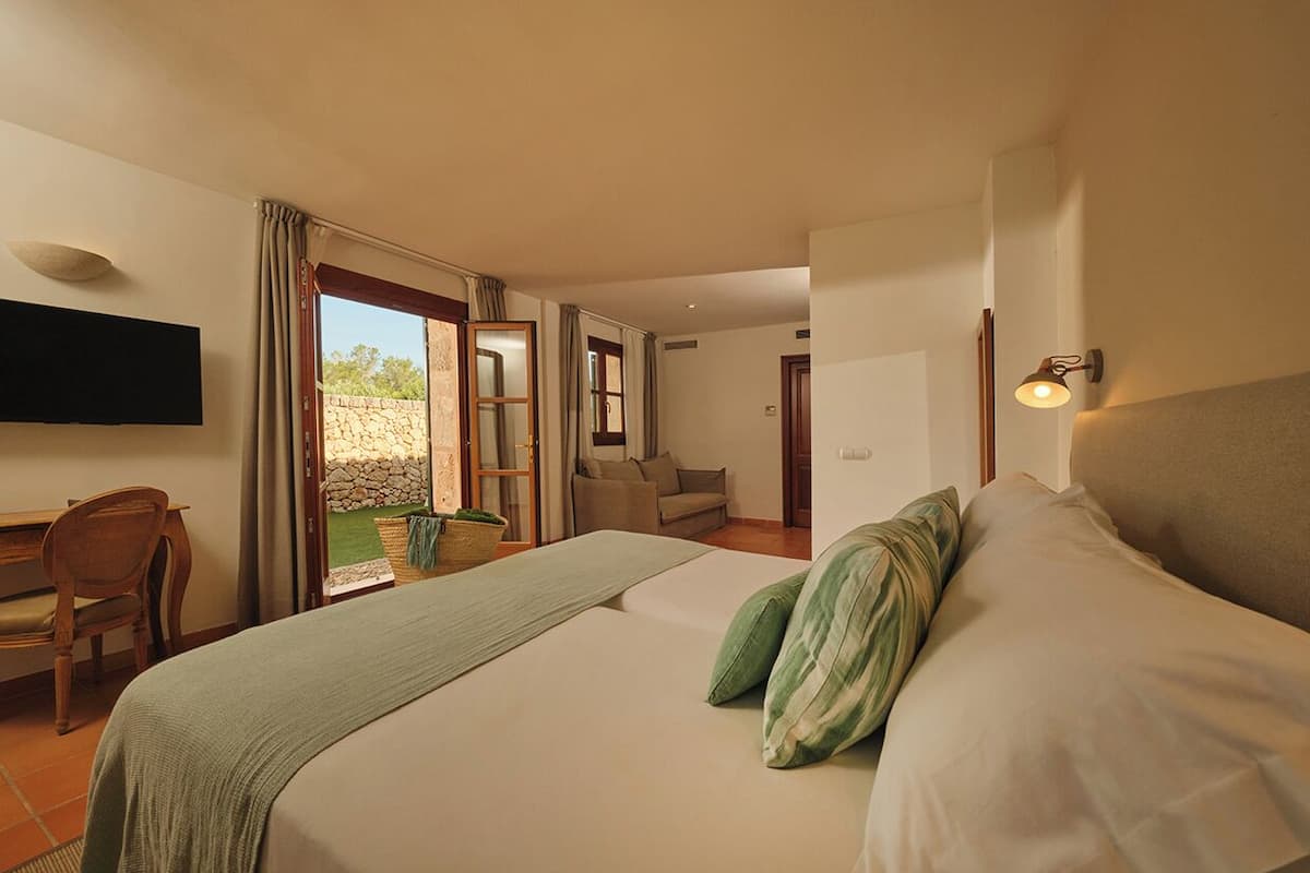 A bedroom with a bed, a desk, a chair, and a TV. There is a door leading to a balcony.