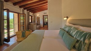 Ein Schlafzimmer mit einem großen Bett, Holzbalken, Blick durch eine Glastür und einer kleinen Sitzecke mit einer Couch.