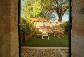 An outdoor patio with a stone wall, green artificial grass, a table and chairs, and a large umbrella.