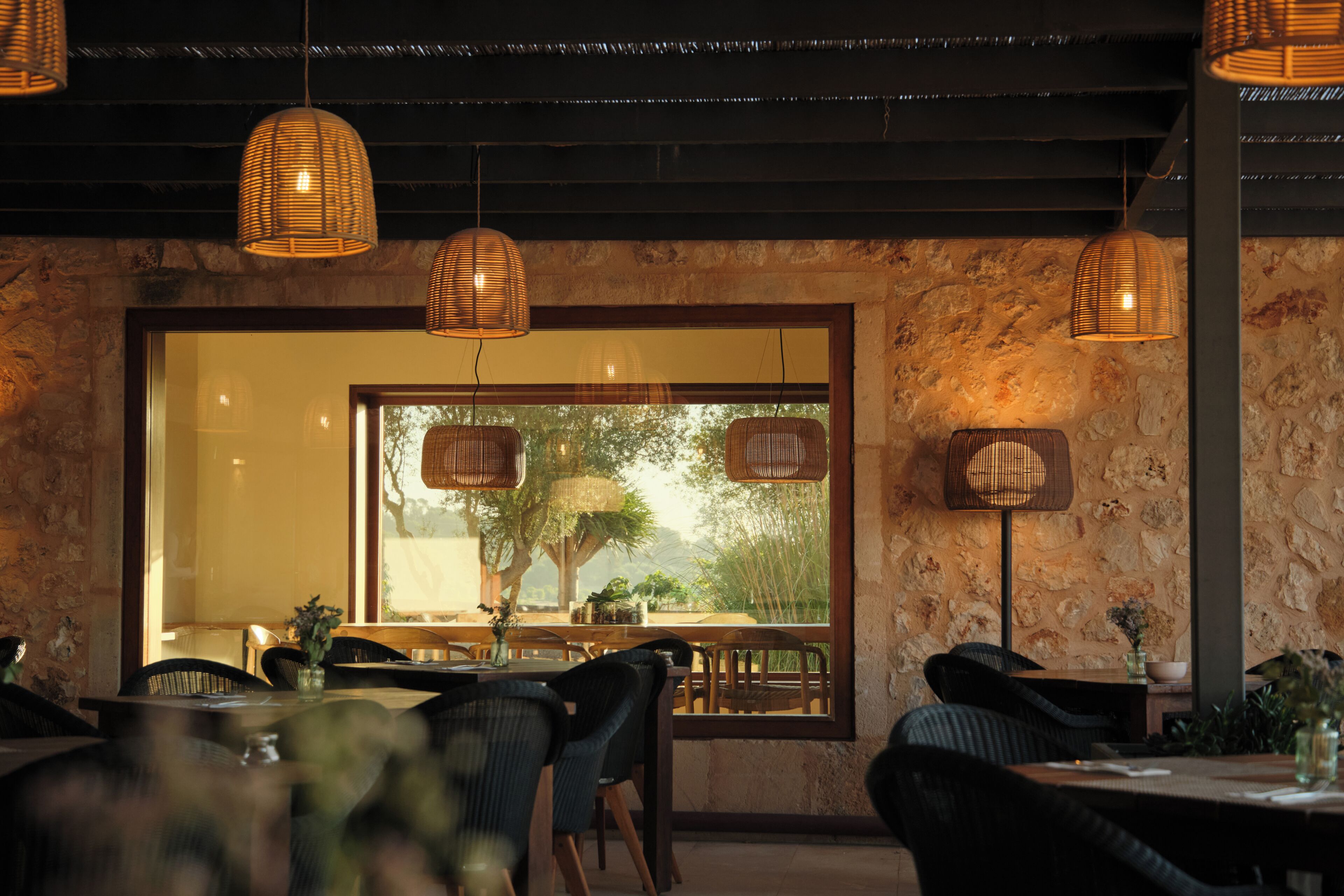 Ein Restaurantinneres mit Korbschwinglampen, Steinwänden und Blick durch ein großes Fenster.