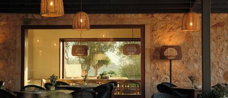 Ein Restaurantinneres mit Korbschwinglampen, Steinwänden und Blick durch ein großes Fenster.