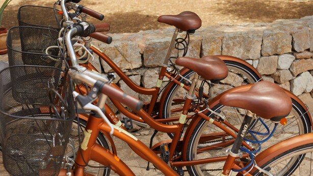 A close-up of a bicycle with a basket and a seat, parked against a stone wall.